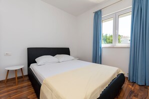 A bedroom with a bed, a small table, and a window with curtains. - Apartments Danijela (Dugi Rat)