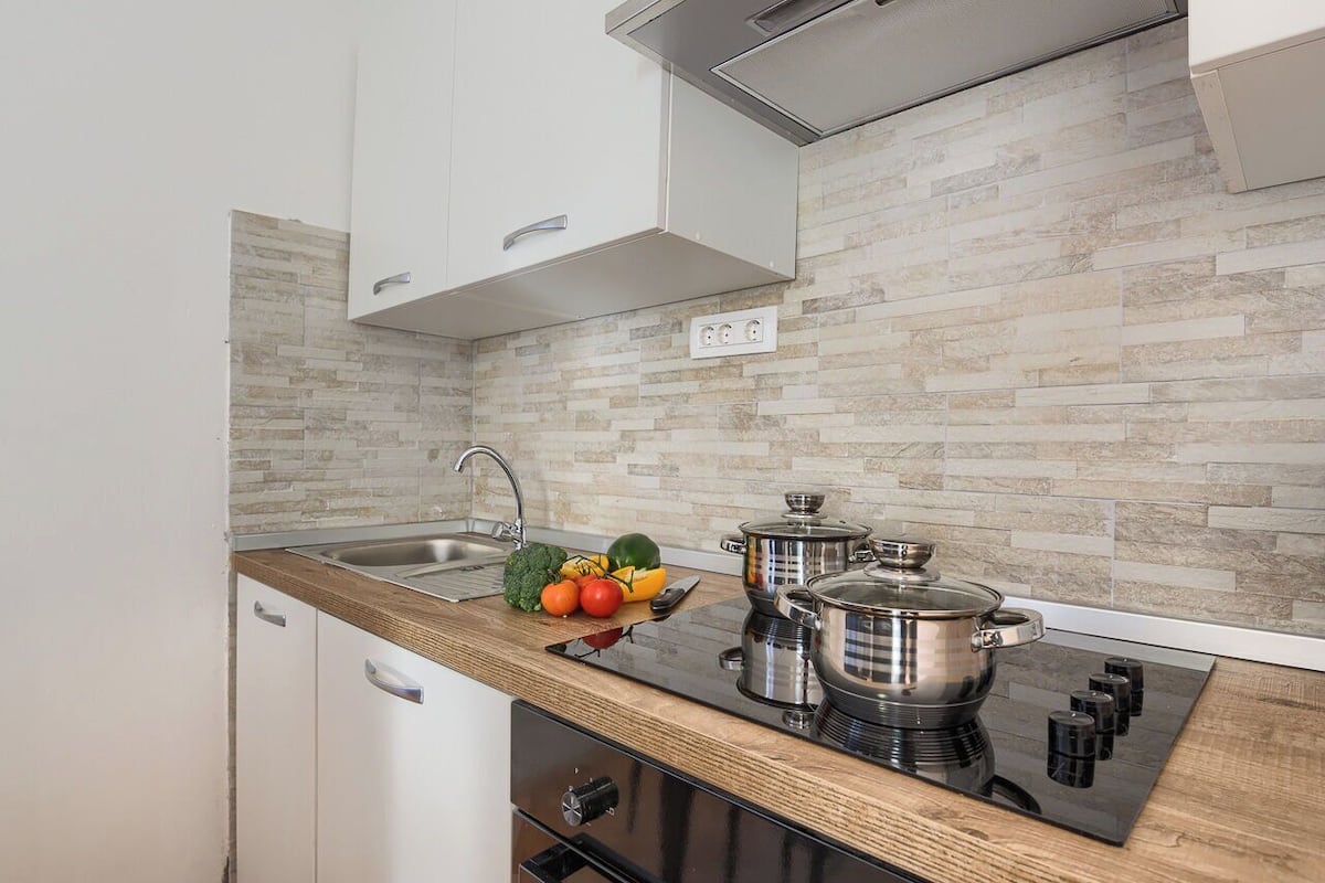 A modern kitchen with a wooden countertop, stainless steel appliances, and a tiled backsplash.