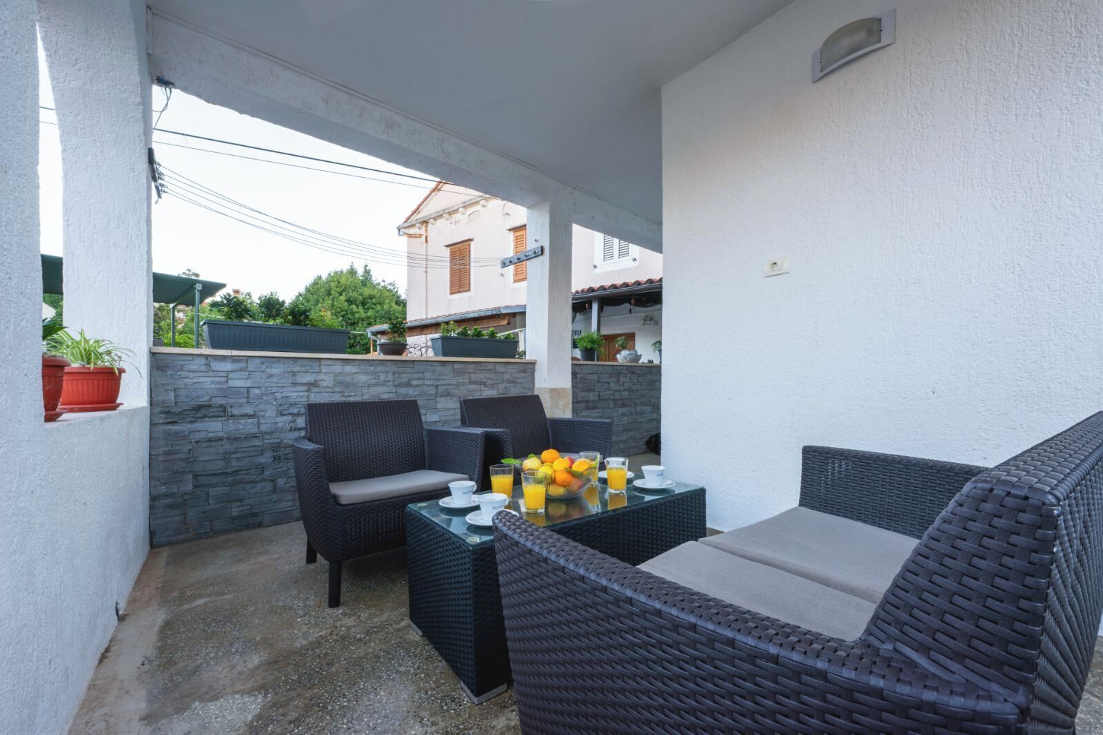 Eine Terrassenausstattung mit Korbmöbeln, einem Tisch mit Früchten und Getränken sowie einer Steinsäule.