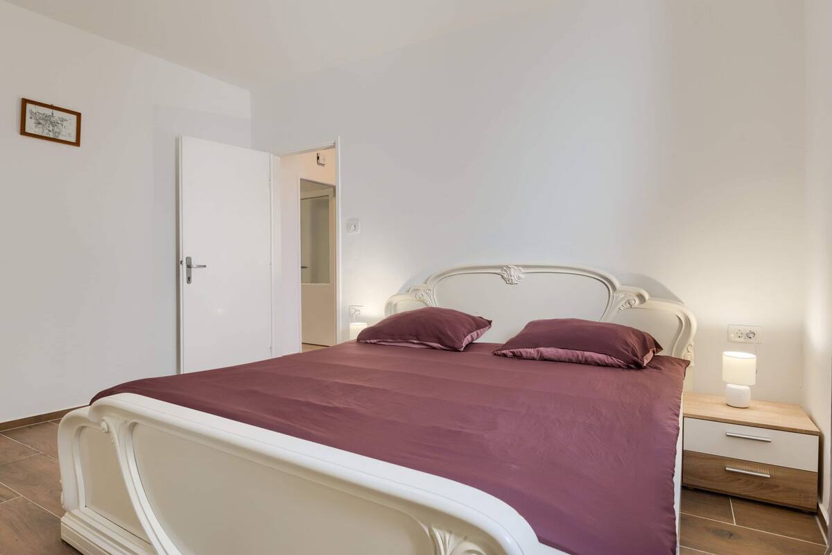 A bedroom with a bed, a nightstand, a lamp, and a door.