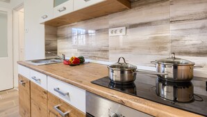 A modern kitchen with wooden cabinets, a black induction cooktop, and stainless steel pots. - Apartment David (Mali Losinj)