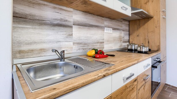 A kitchen with a stainless steel sink, wooden countertop, and white cabinets. - Apartment David (Mali Losinj)