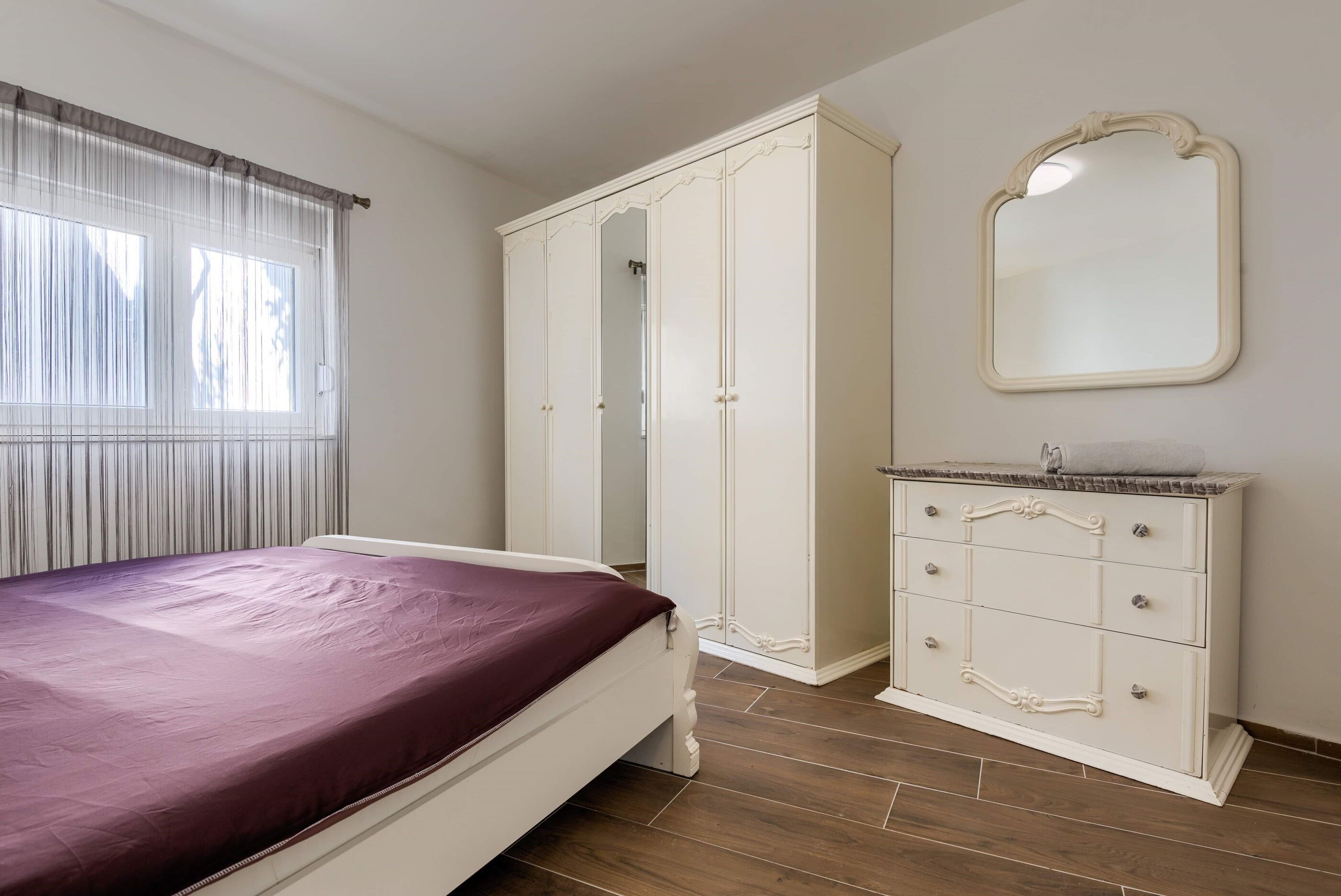 A bedroom with a bed, a wardrobe, a dresser, and a mirror.