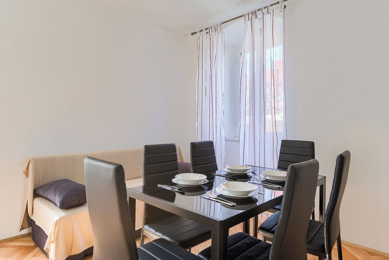 A modern dining area with a glass table, black chairs, and a sofa with cushions.