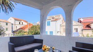 A balcony with wicker furniture, a table with fruit and drinks, and a view of buildings with red roofs. - Apartment David (Mali Losinj)