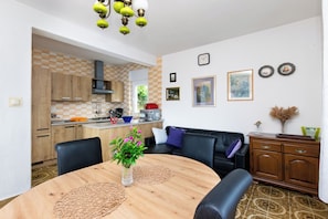 Un salon moderne avec une table ronde en bois, un canapé en cuir noir et un coin repas agrémenté d’un mur recouvert de carreaux à motifs géométriques.