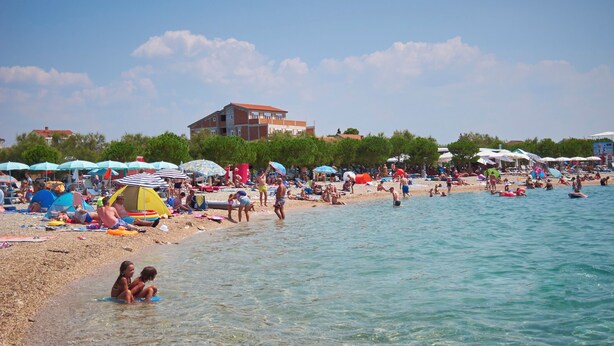 A crowded beach with people sunbathing and swimming, tents, and umbrellas. - Apartment Sunshine (Vodice)
