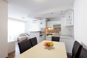 Egy modern konyha fehér szekrényekkel, mikrohullámú sütővel és egy étkezővel, ahol egy két személyre megterített asztal található.