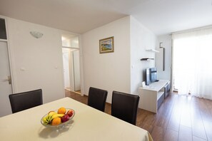 A dining area with a table set for two, a bowl of fruit, and a TV on a stand. - Apartment Srecko (Omis)