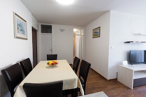 A dining area with a table set for six, a bowl of fruit, and a TV on a stand. - Apartment Srecko (Omis)