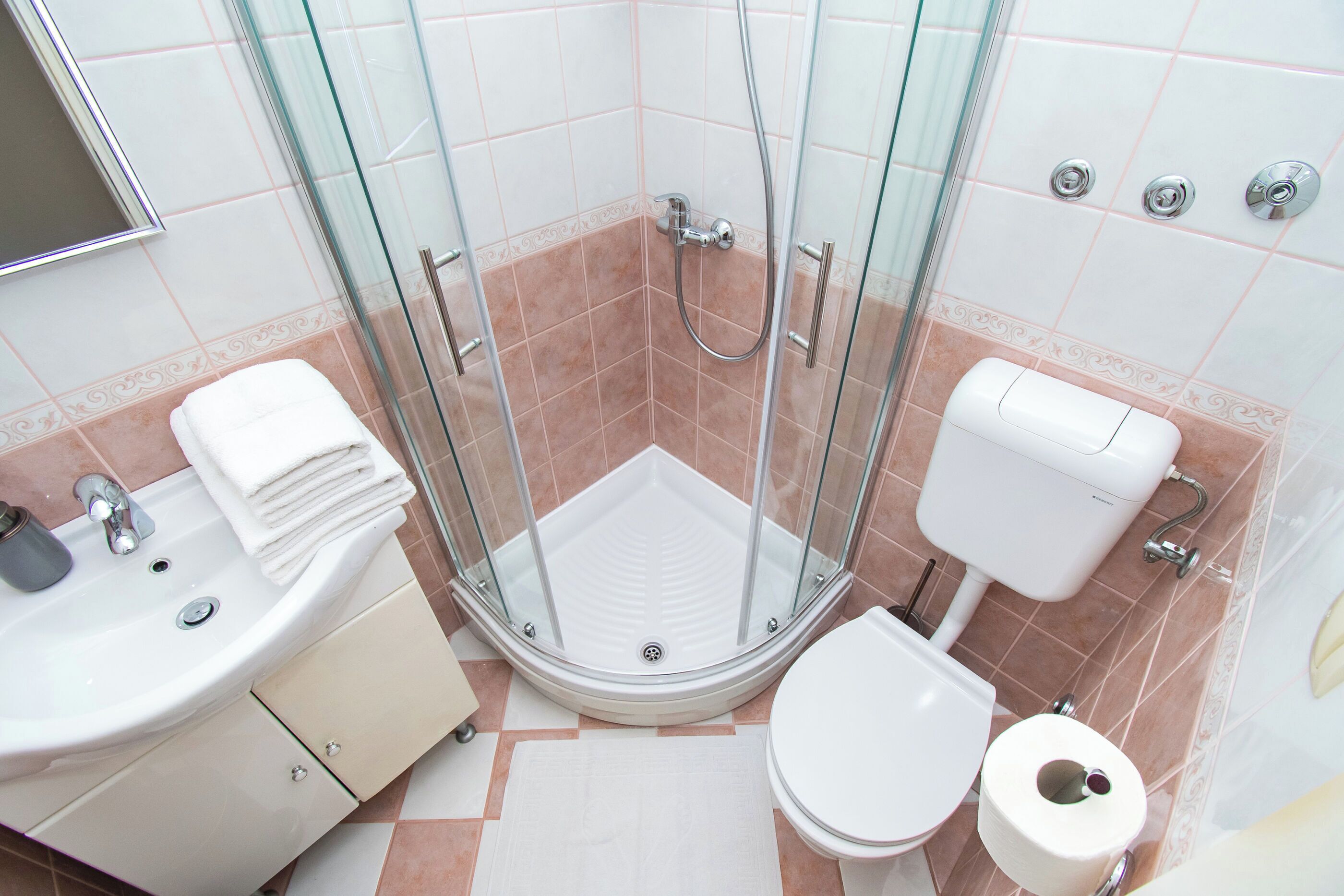 Een badkamer met een douchecabine van glas, een wastafel met spiegel, toilet en een stapel witte handdoeken.