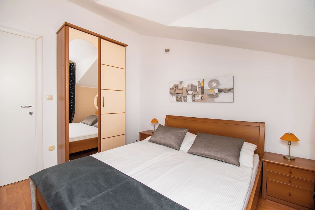 A bedroom with a bed, a wardrobe, a nightstand, a lamp, and a wall art piece.