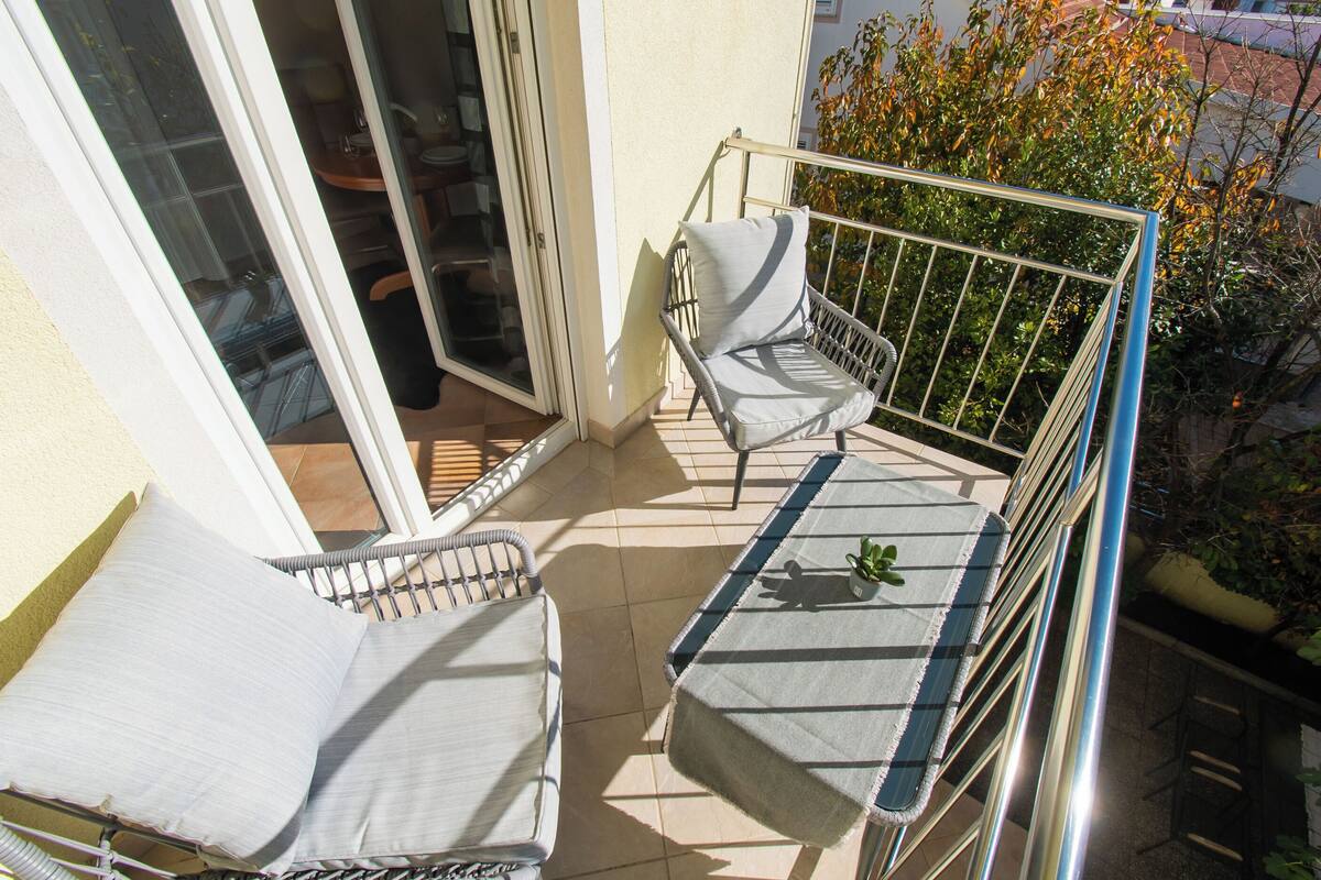 A balcony with two wicker chairs, a small table, and a metal railing.