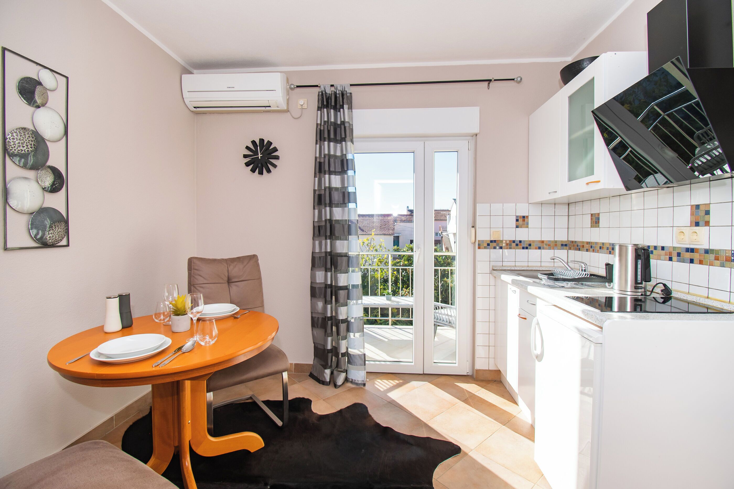 A compact living space with a dining area, kitchenette, and a sliding glass door leading to an outdoor balcony.