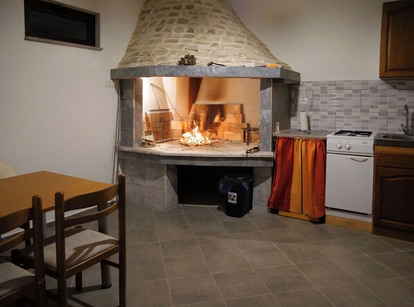A kitchen with a stone-built oven, a dining table with chairs, and a small white appliance. - House Luketini Dvori (Marina)