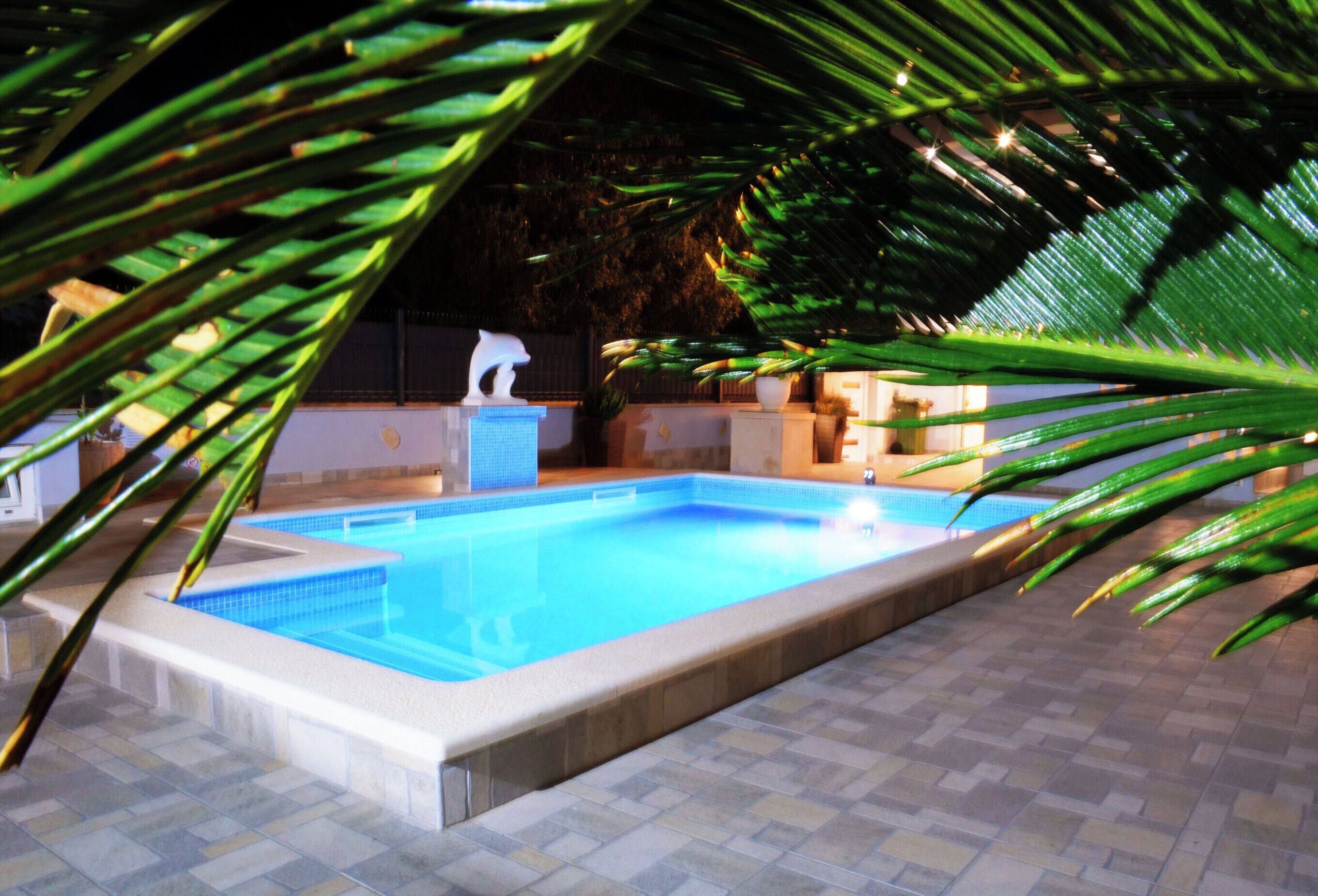 A rectangular swimming pool with a tiled edge, surrounded by a tiled patio area.