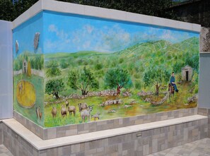 A mural of a pastoral scene with a man on a donkey, sheep, and a stone house. - House Luketini Dvori (Marina)
