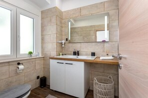 Ein modernes Badezimmer mit Waschtisch aus Holz, einem großen Spiegel und einer Toilette.