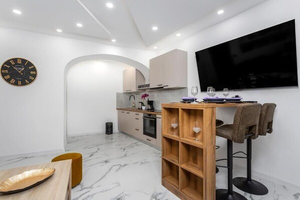Eine moderne Küche mit Einbauofen, einem Holztisch mit Barhocker und einem großen Flachbildfernseher an der Wand.