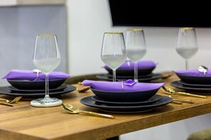 Ein Esstisch, gedeckt mit schwarzen Tellern, violetten Servietten und klaren Weinkellen.