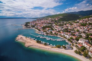 Ein Luftbild einer Küstenstadt mit einem Yachthafen, Wohnhäusern und einem Bergpanorama im Hintergrund.