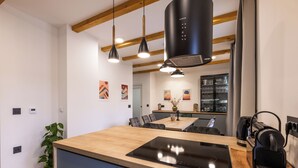 A modern kitchen with a central island, pendant lights, and a built-in stove. - House Vuk (Ravna Gora)