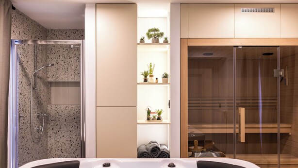 A modern bathroom with a glass-enclosed shower, a built-in bathtub, and shelves with plants and toiletries. - House Vuk (Ravna Gora)