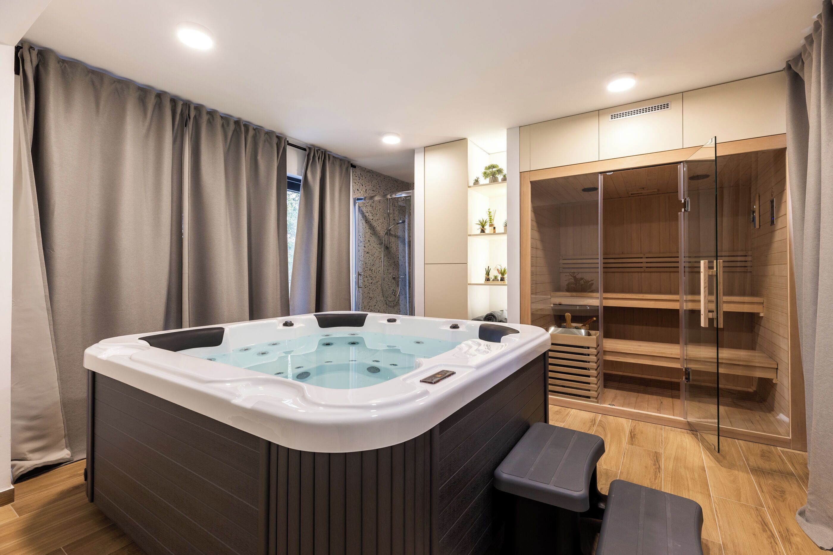 A modern bathroom with a large bathtub, a glass shower enclosure, and a wooden sauna area.