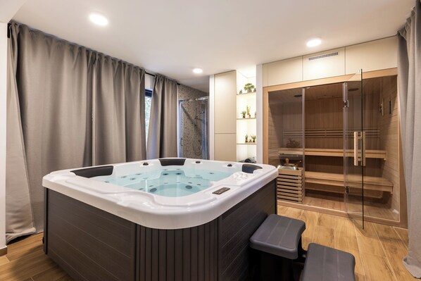 A modern bathroom with a large bathtub, a glass shower enclosure, and a wooden sauna area. - House Vuk (Ravna Gora)