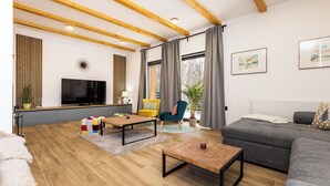 A modern living room with a flat-screen TV, wooden flooring, a grey sofa, and a yellow chair. - House Vuk (Ravna Gora)