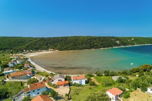 An aerial view of a coastal village with houses, a beach, and a boat in the water. - Apartments Zeljko (Rab)