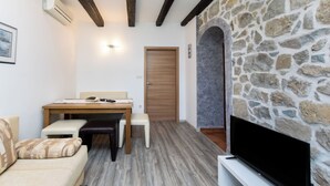 A cozy living room with a stone wall, a flat-screen TV, a wooden dining table, and a sofa. - Apartments Zeljko (Rab)