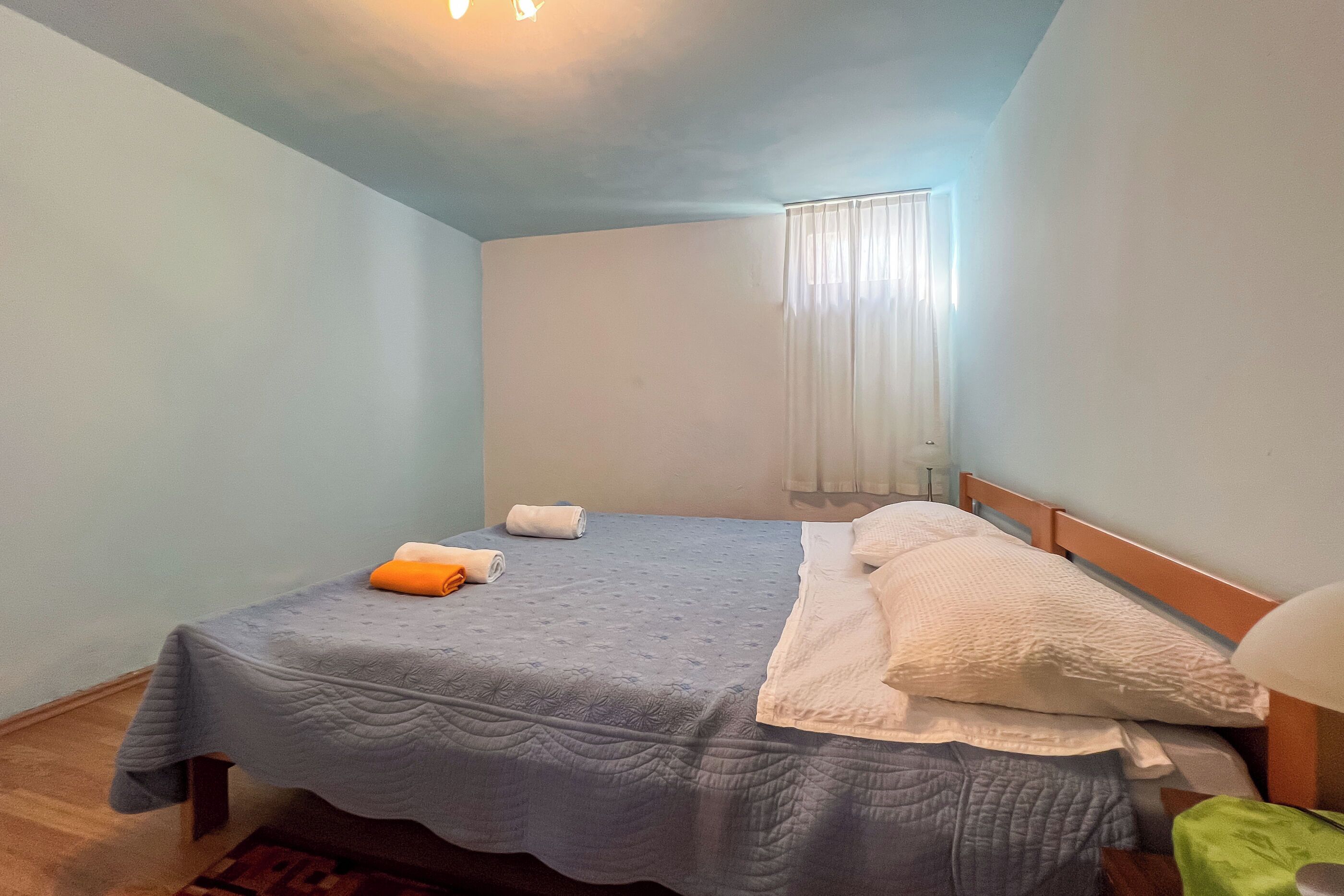 A single bed with a blue quilt, white pillows, and a green blanket.