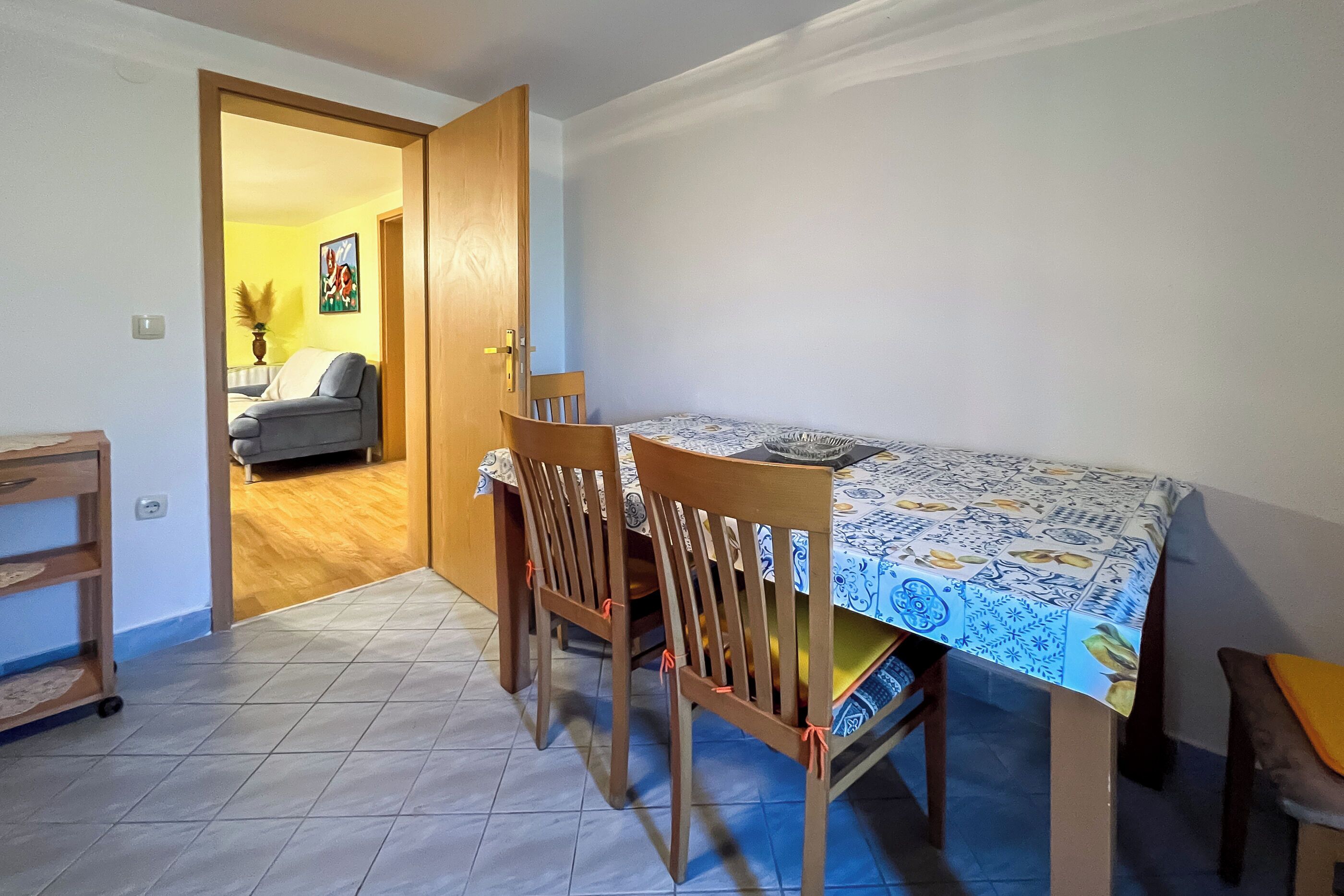 A dining area with a table covered by a patterned tablecloth, wooden chairs, and a door leading to another room.