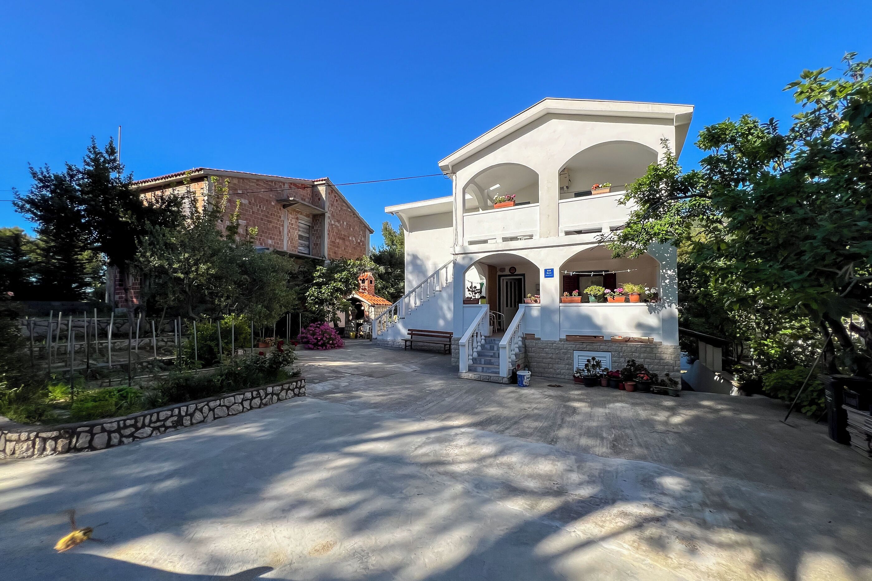 A two-story building with a central entrance, a stone wall, and a paved driveway.