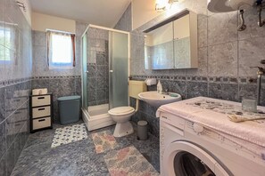A bathroom with a shower, toilet, sink, and washing machine. - Apartments Franjo (Rab)