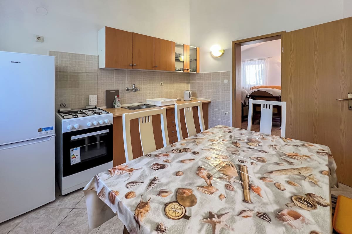 Une cuisine compacte équipée d’une cuisinière, d’un four et d’un évier. On y trouve une table à manger recouverte d’une nappe ornée de motifs représentant des créatures marines.