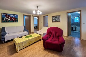 A living room with a sofa, a red chair, a table with a yellow tablecloth, and a chandelier. - Apartments Franjo (Rab)