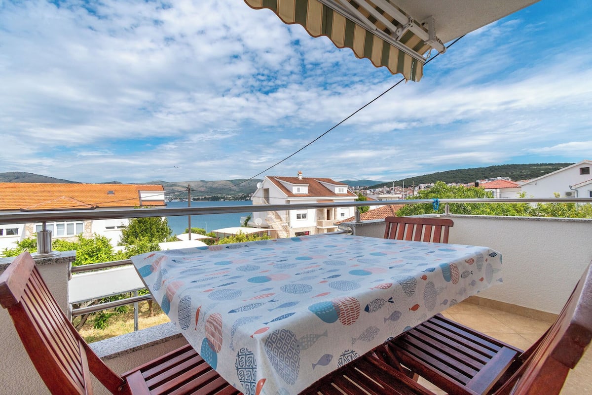 Un balcon avec une table et des chaises, donnant sur une étendue d’eau et des bâtiments.
