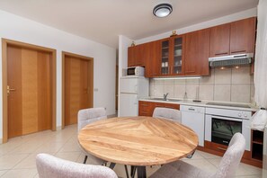 A modern kitchen with wooden cabinets, a microwave, a dishwasher, and an oven. There is a round wooden table with four chairs. - Apartments Ivan (Okrug)