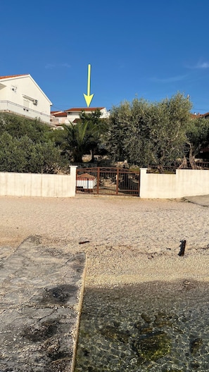 A gravel parking area with a gated entrance, a building with a red roof, and a clear blue sky. - Apartments Ivan (Okrug)