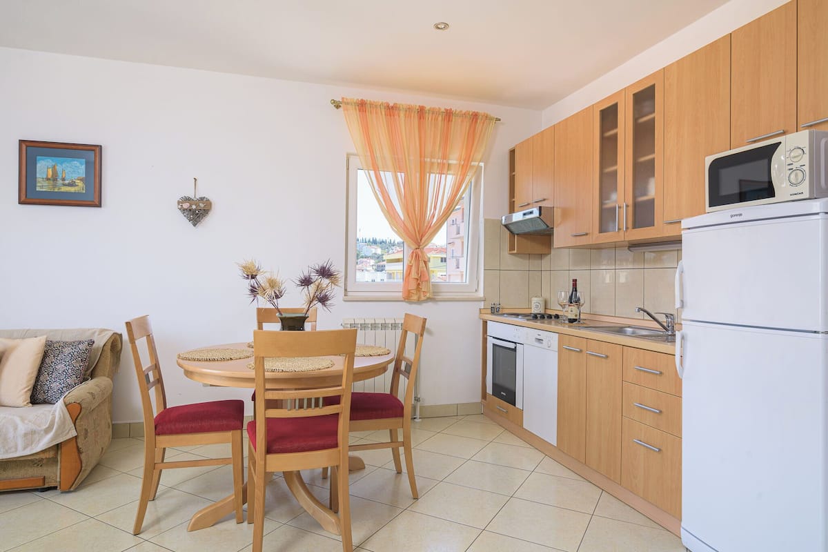 Une cuisine de taille réduite, dotée de meubles en bois, d’un réfrigérateur blanc et d’un coin repas avec une table et des chaises.