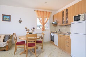 Een kleine keuken met houten kastjes, een witte koelkast en een eethoek met een tafel en stoelen.