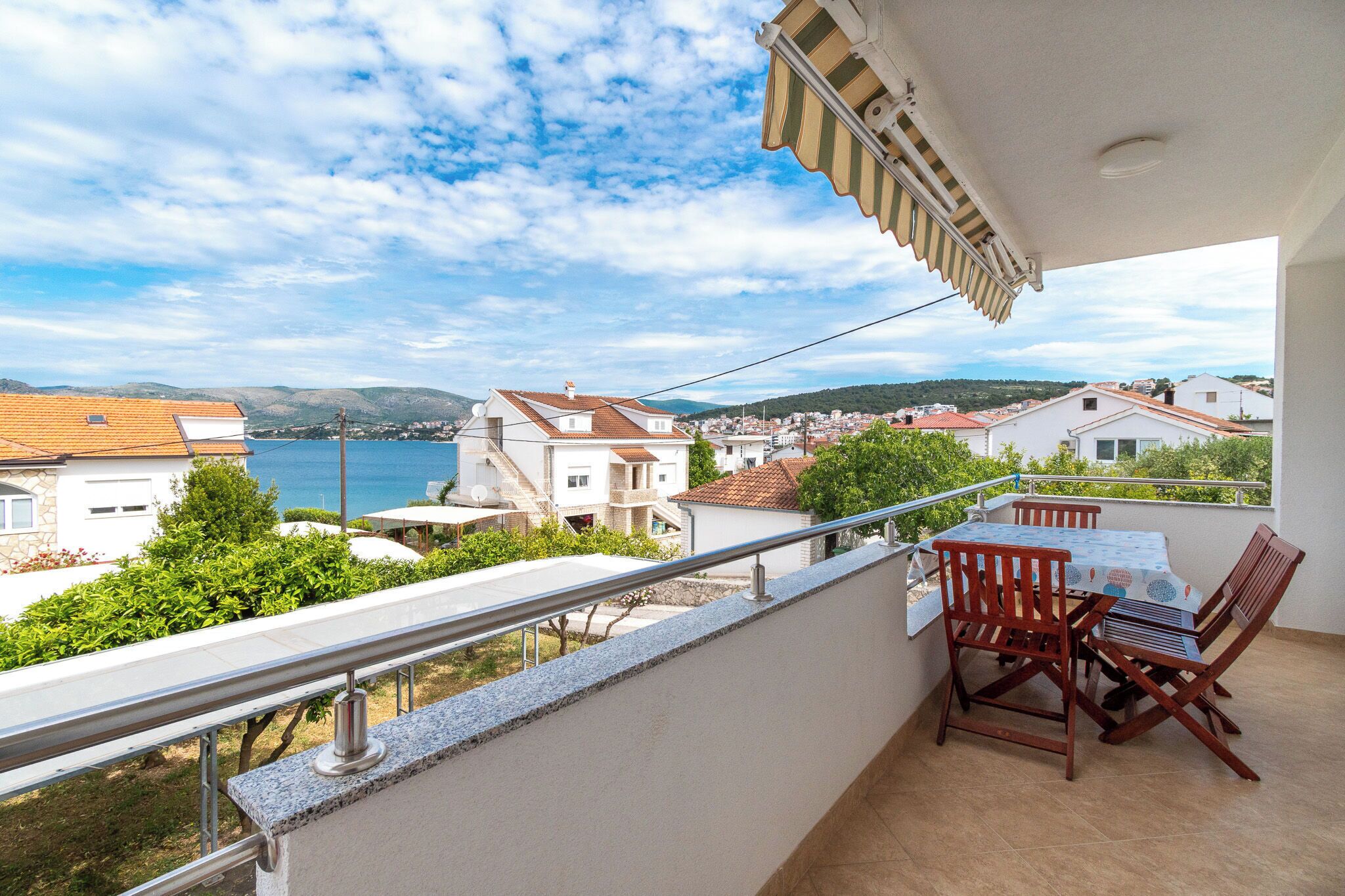 Een balkon met een tafel en stoelen, met uitzicht op een kustplaatsje met huizen en de zee.