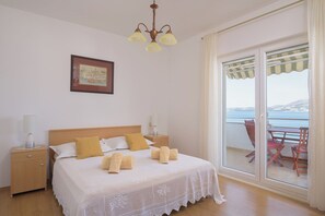 Una camera da letto con un letto, comodini, un lampadario, un quadro incorniciato e un balcone con tavolo e sedie.