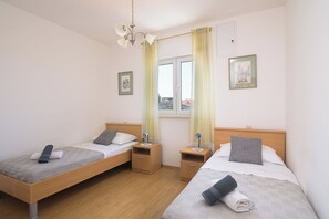 Ein Doppelzimmer mit zwei Betten, Nachttischen, einem Fenster mit Vorhängen und einer Deckenleuchte.