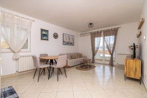 A living room with a sofa, dining table, chairs, a small coffee table, and a TV stand. - Apartments Ivan (Okrug)