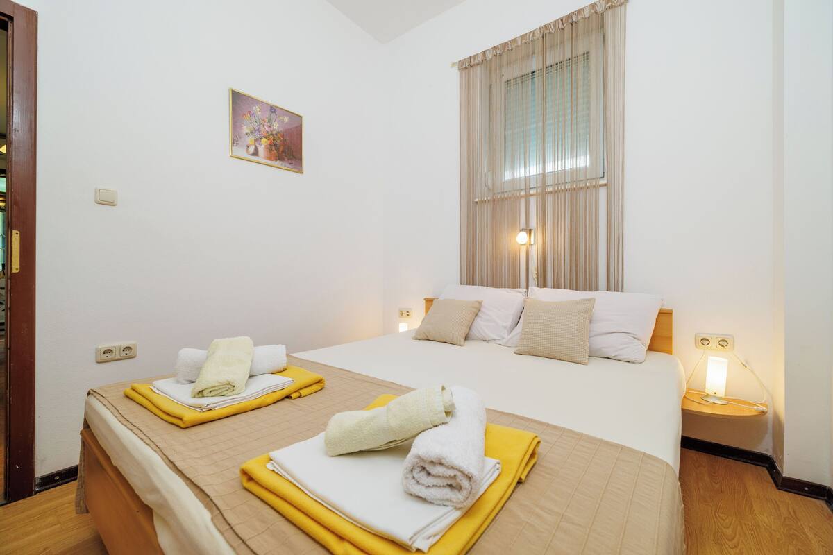 Ein Hotelzimmer mit Bett, Nachttischen, einer Lampe, einem Bild an der Wand und einem Fenster mit Vorhängen.