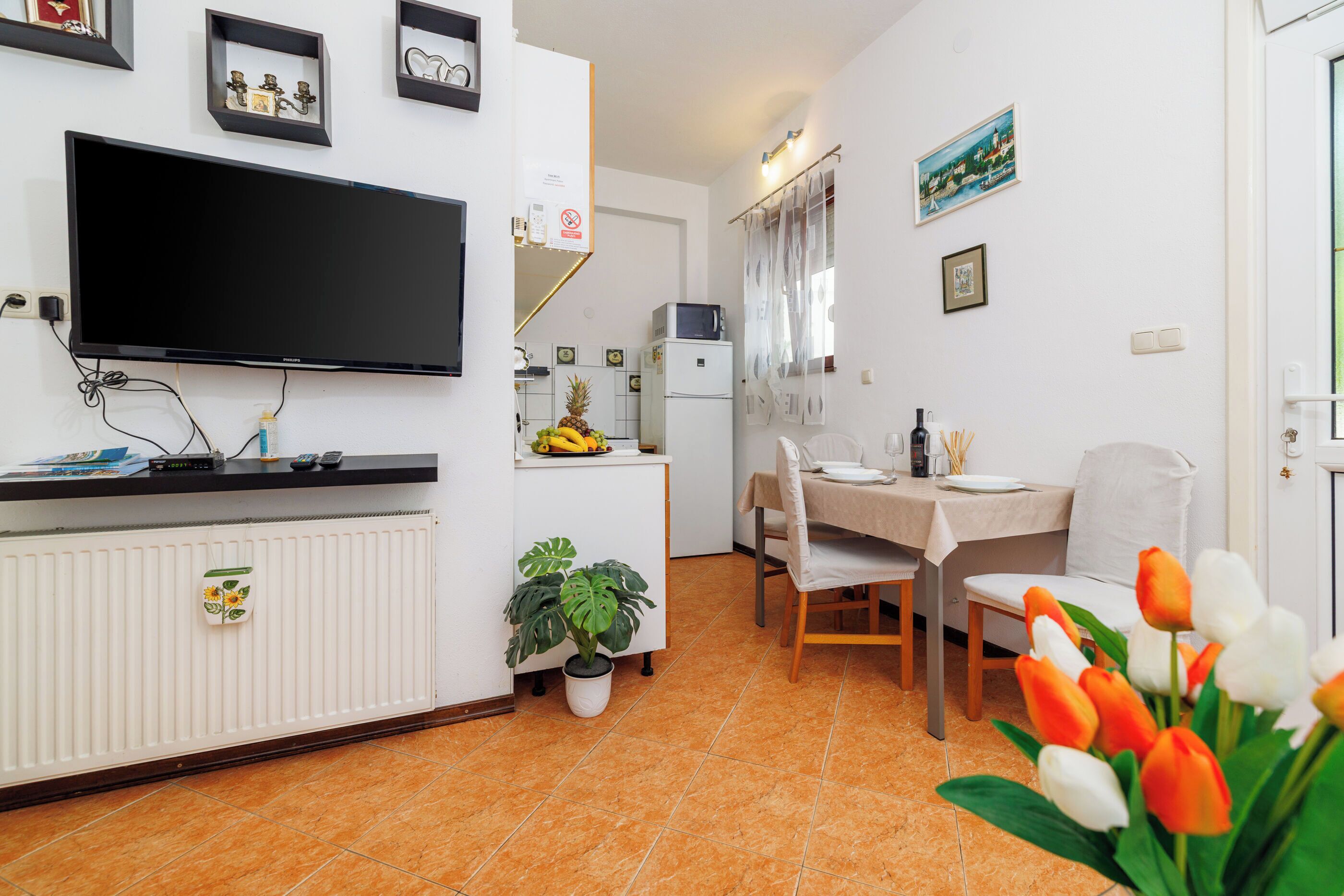 A modern kitchen with a flat-screen TV, white cabinets, and a dining area with a table and chairs.