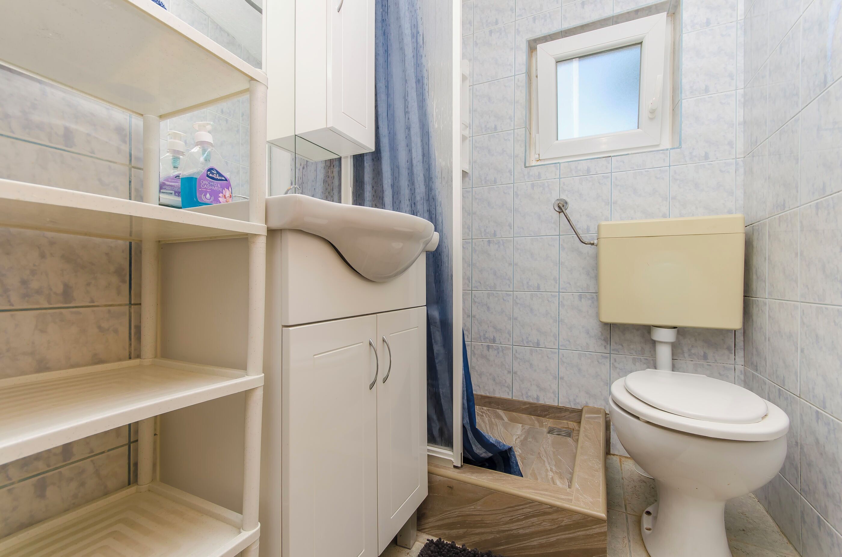 Un bagno con il water, uno scaffale con articoli da toilette e una finestra.